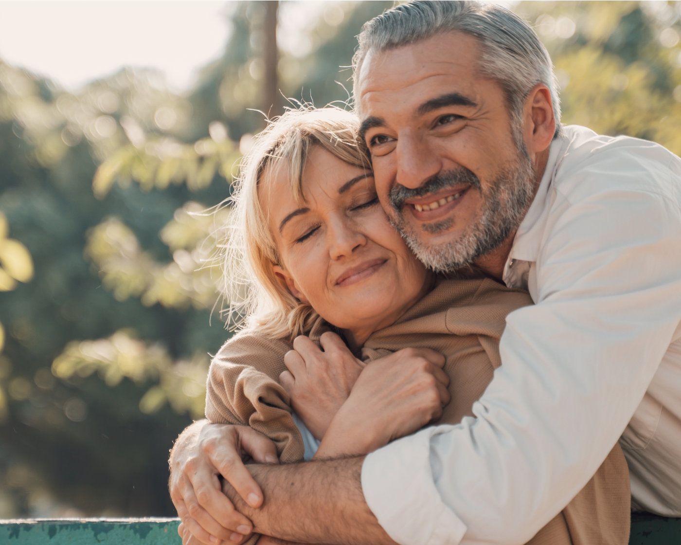 Happy man and woman outside hugging on green park bench.