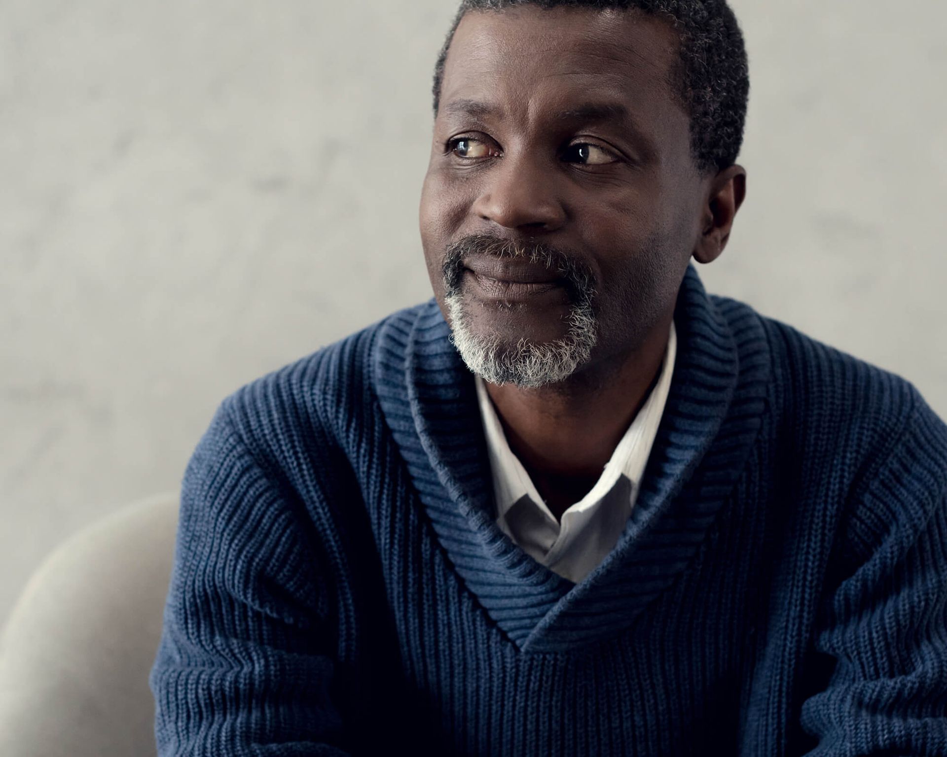 Man sitting in chair wearing a blue sweater glacing to his right.