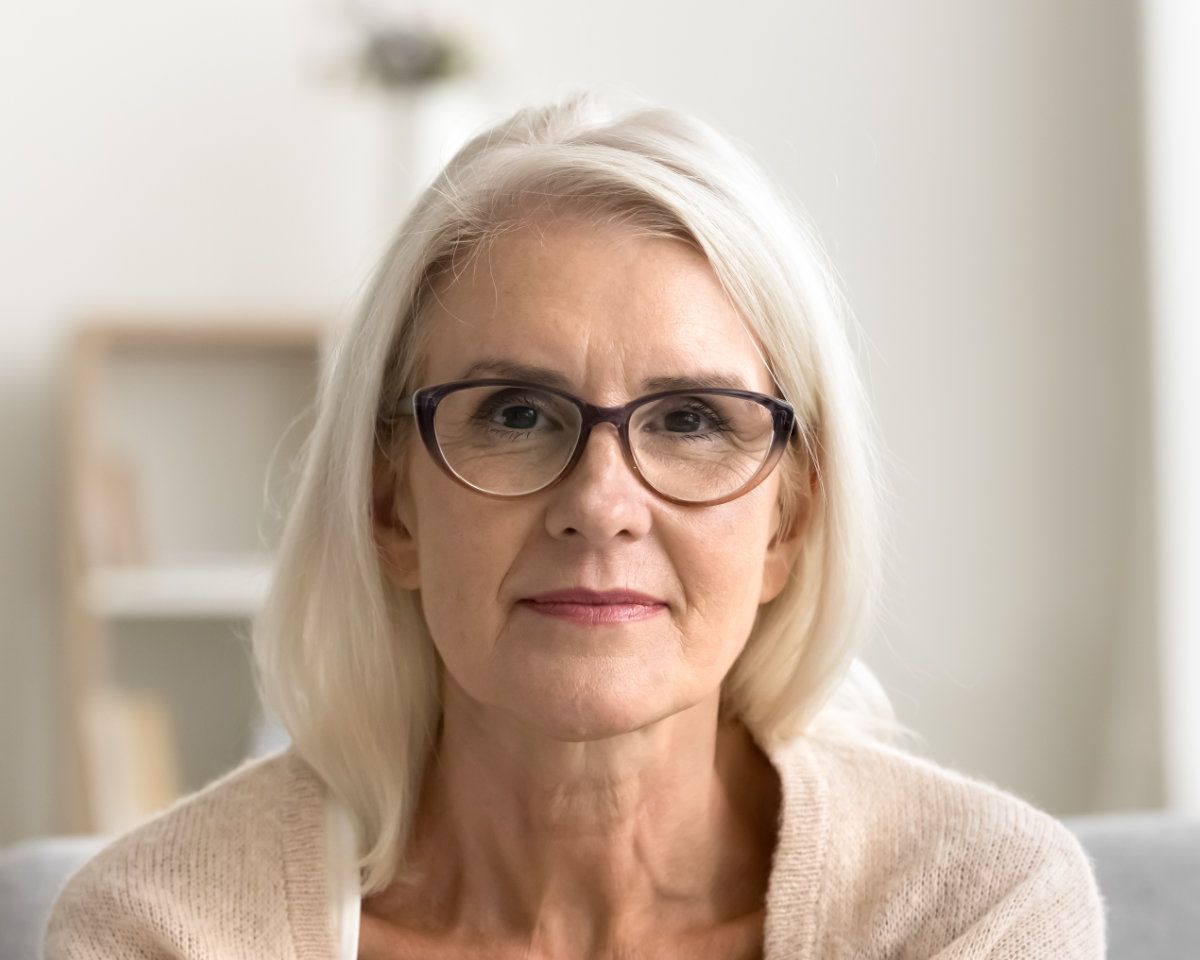 Woman sitting inside looking at camera and wearing a beige cardigan sweater.