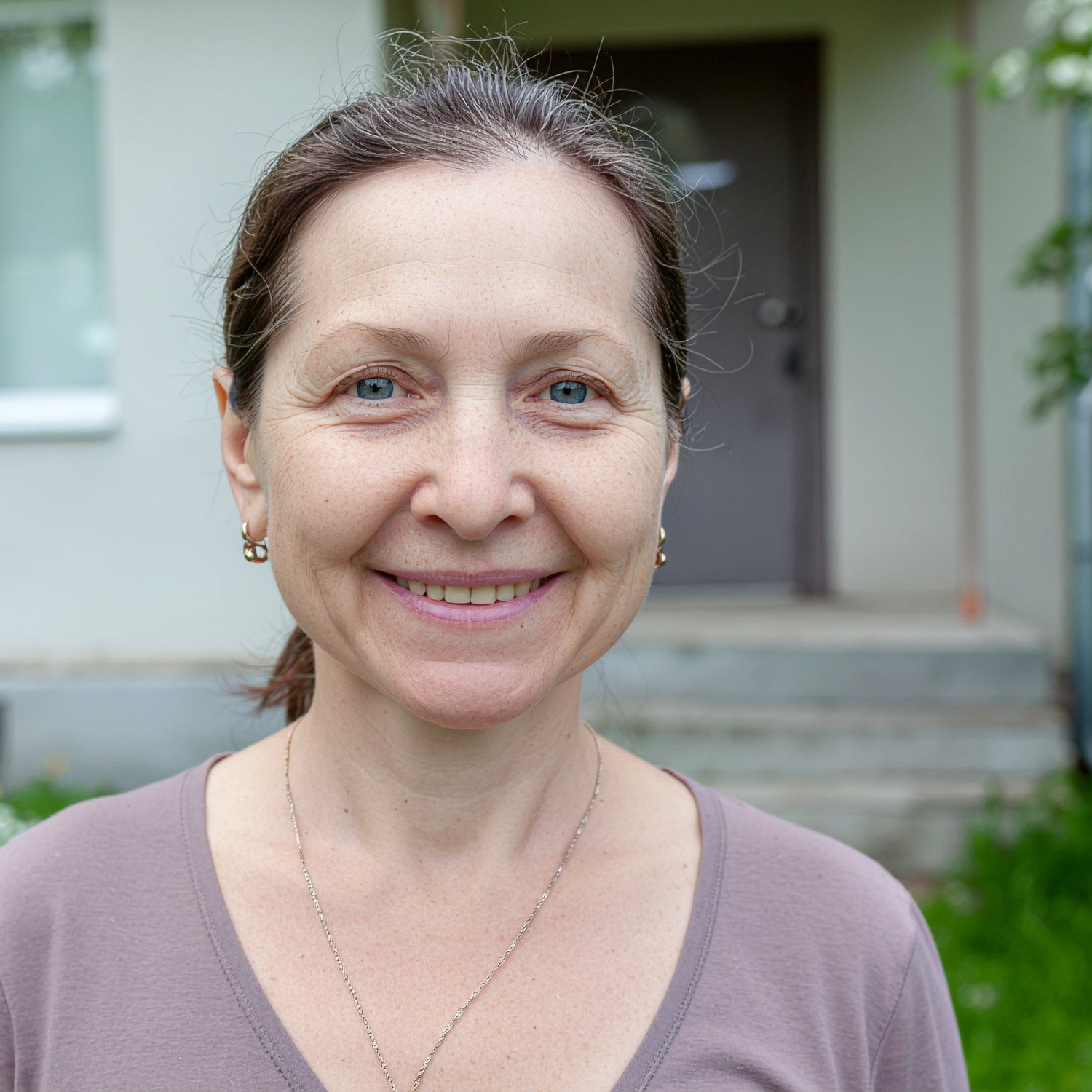 Woman standing outside house with hair pulled back in ponytail.
