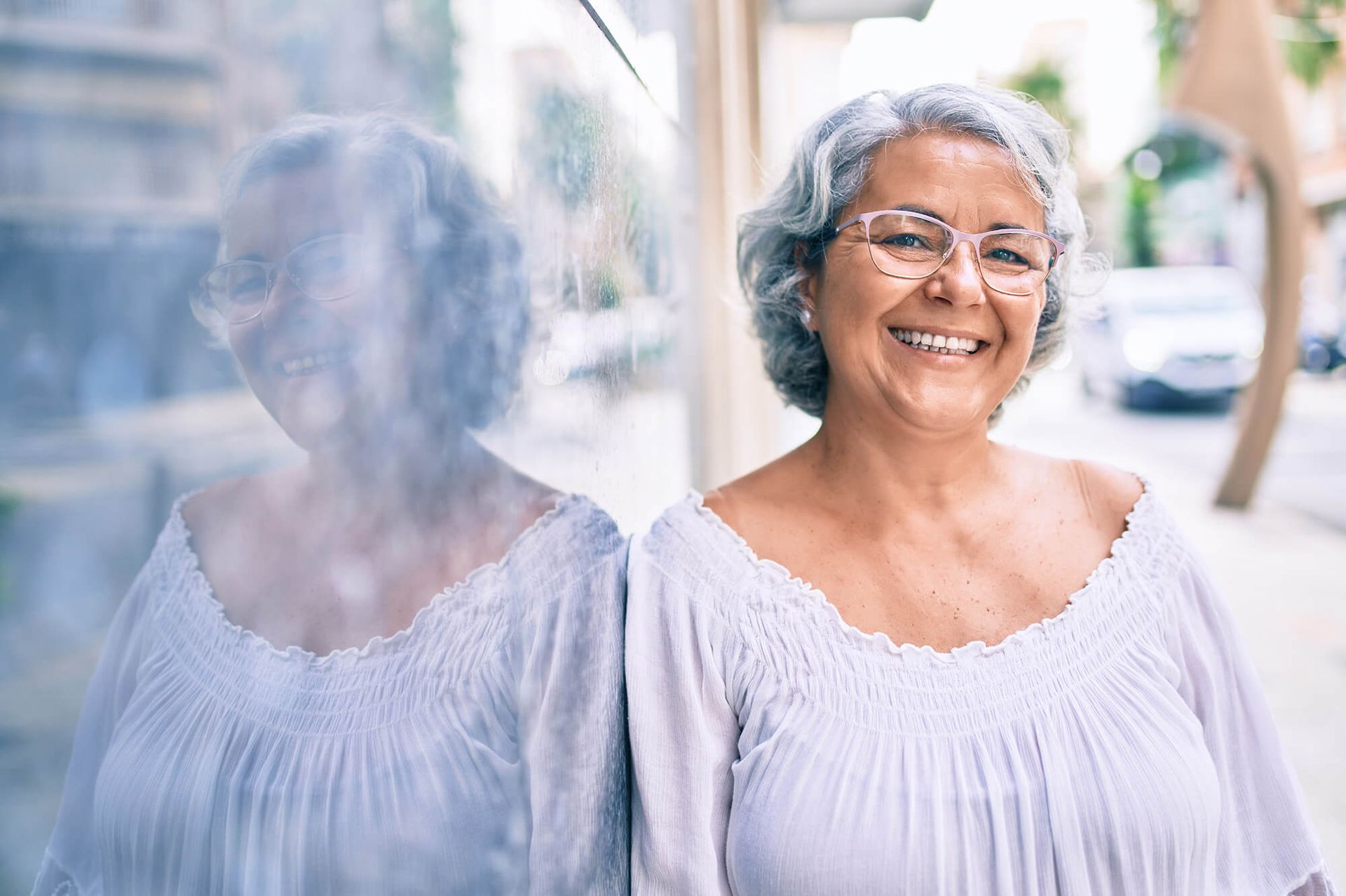 Happy middle-aged woman standing outside on the sidewalk next to a building.