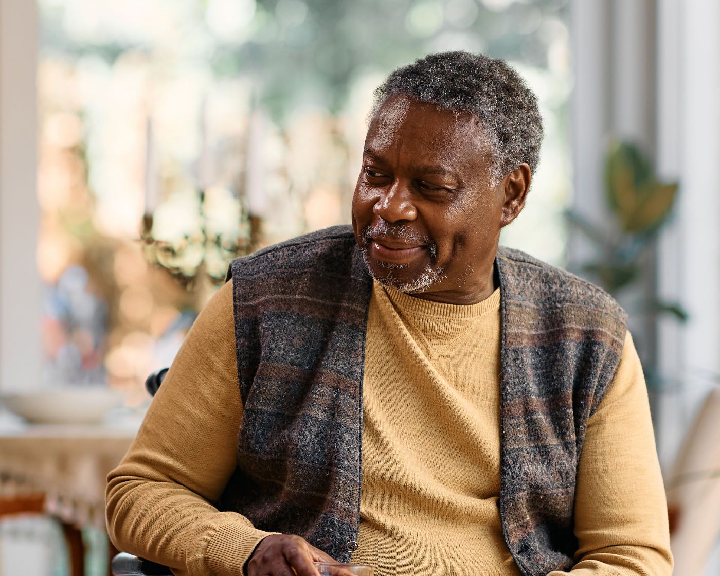 A smiling middle-aged man wearing a sweater and vest sitting in a wheelchair looking to his right.
