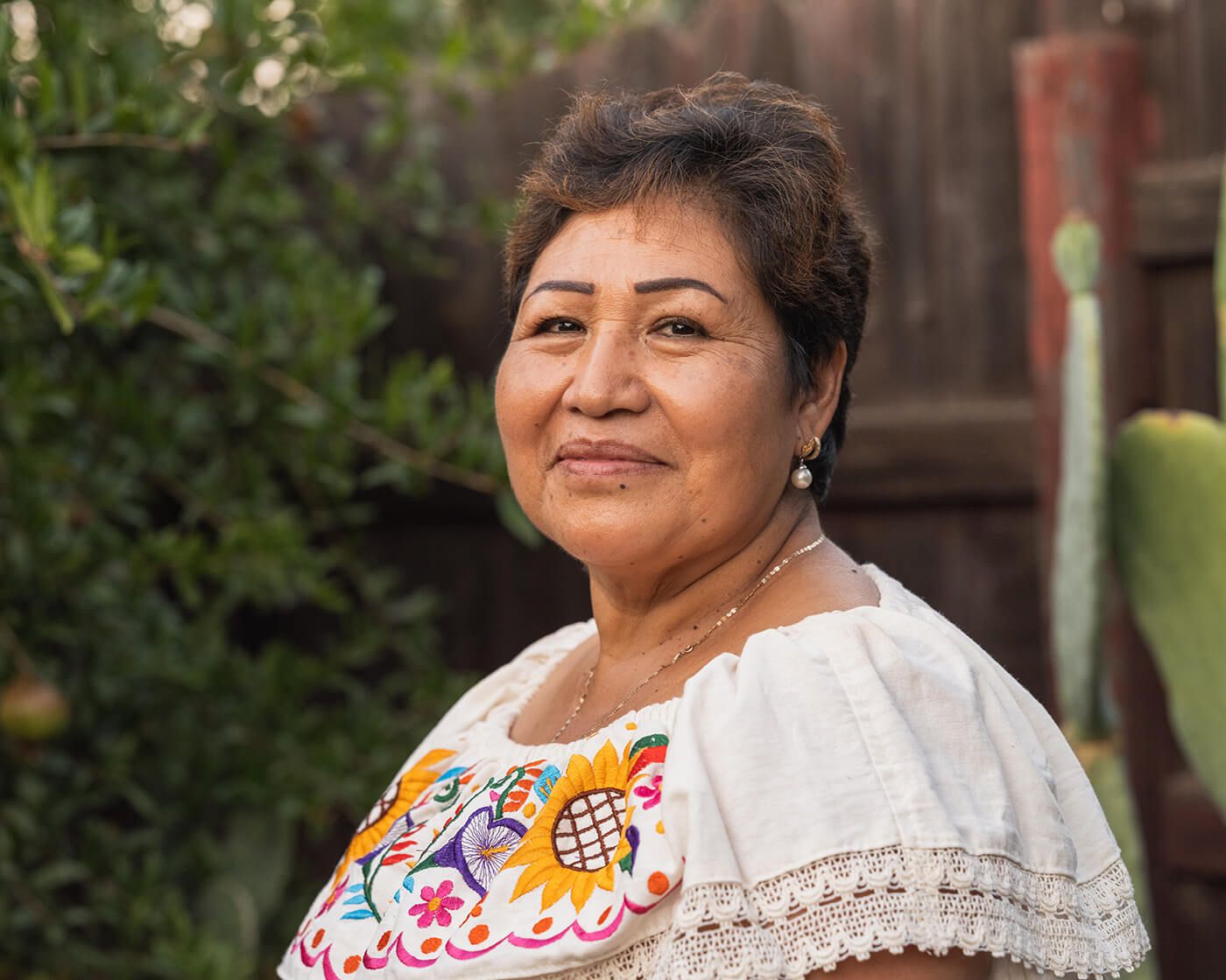 Woman standing outside in front of a wooden fence and a bush.