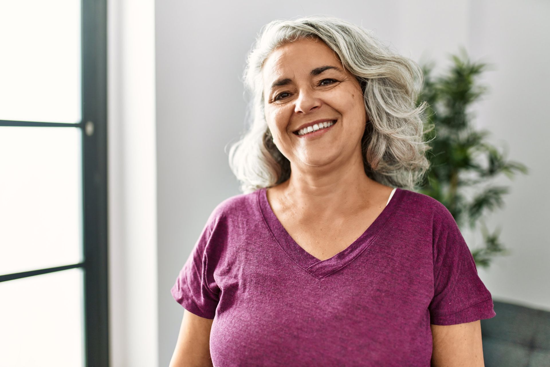 MIddle age woman with long gray hair wearing maroon v-neck shirt smiling at the camera